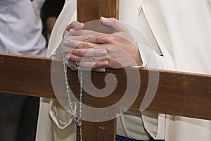 Penitent supports their hands crossed with a rosary on a wooden cross in holy week photo
