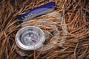 Penknife and compass on forest floor of pine needles