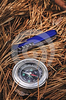 Penknife and compass on forest floor of pine needles