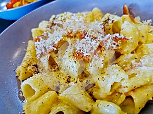 Penne pasta carbonara on white sauce with bacon and extra topping cheese served on blue plate