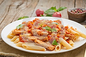 Penne pasta, chicken or turkey fillet, tomato sauce with basil leaves on old rustic wooden background. Close up, side view