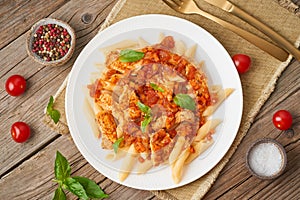 Penne pasta, chicken or turkey fillet, tomato sauce with basil leaves on old rustic wooden background. Top view