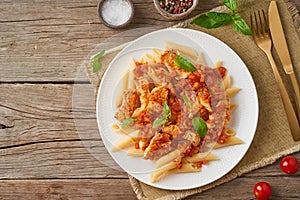 Penne pasta, chicken or turkey fillet, tomato sauce with basil leaves on old rustic wooden background. Top view, copy space