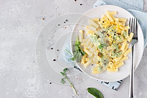 Penne pasta with green cream sauce, cheese and micro greens on a ceramic plate, light grey stone background.