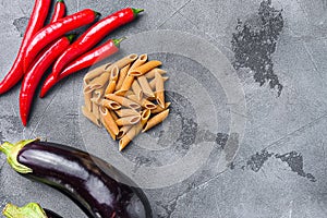 Penne pasta ingredients eggplant pasta, pepper tomatoe sauce, on grey background stop view space for text