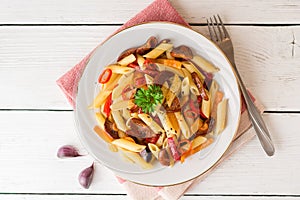 Penne pasta with mushrooms, bell pepper, chilli and parsley on white plate on white wooden background.