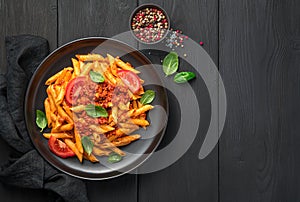 Penne pasta with tomato and meat bolognese sauce and fresh basil on a black background.