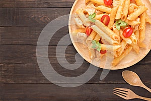 Penne pasta in tomato sauce with chicken on a wooden background.