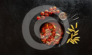 Penne pasta with tomato sauce and green basil decorated in a iron pan on a black background. Top view with copy space