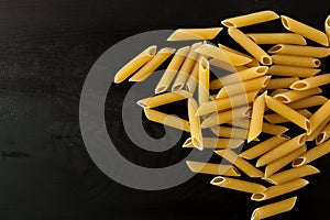 Penne Raw penne italian pasta on a wood black textured background. Close-up view from the top. Free space for text.