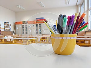 Pens and pencils on a teacher`s desk in primary school classroom