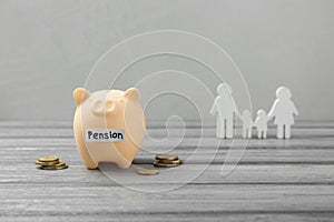 Pension savings. Piggy bank, coins and figures of family on grey wooden table, space for text