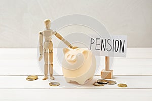 Pension savings. Piggy bank, coins and mannequin on white wooden table