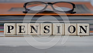 PENSION - word on wooden cubes on the background of a folder with documents and glasses