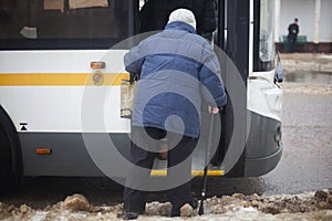 Pensioner enters bus. Old woman in Russia. Grandmother with stick for support when walking. Human and walking problems