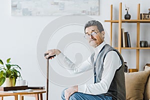 Pensioner holding walking cane and sitting