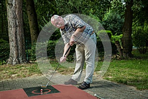 Pensioner at a minigolf court has a lot of fun during his shot.