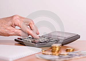 A pensioner sums up his money on a calculator. Hand of an old woman and a calculator close-up