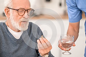 Pensioner taking a pill with water supervised by his caregiver