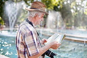 Pensioner tourist in hat searching for destination on map in par