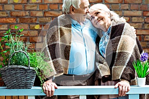 Pensioners smiling while standing in plaid blankets near flower pots