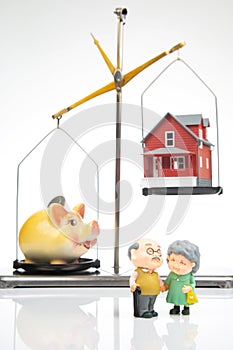 Pensioners stand near a piggy bank with a house on the scales. The concept of accumulating finances to buy a house for living.