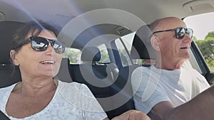 pensioners on vacation, cheerful old husband and wife having fun singing and dancing in the car while traveling