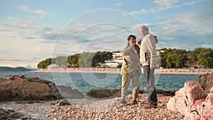 pensioners on vacation, an elderly man and an old woman are having fun throwing pebbles into sea while standing on shore