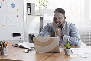 Pensive african american businessman looking at laptop screen at workplace.