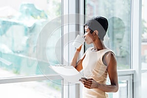 Pensive african american businesswoman with clipboard drinking coffee in office