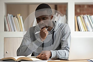 Pensive african American guy reading textbook studying