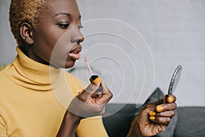 Pensive african american woman applying lip gloss and looking