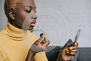 Pensive african american woman applying lip gloss and looking photo