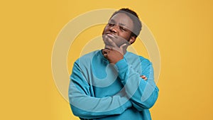 Pensive African man thinking making difficult decision solving problem posing isolated on orange