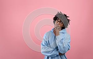 Pensive Afro teen guy touching his chin, thinking over something on pink studio background, copy space