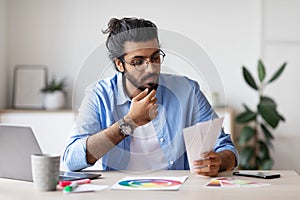 Pensive Arab Designer Looking At Color Swatches While Working In Office