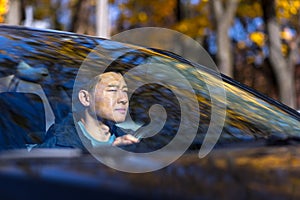 A pensive Asian man is sitting in the car, the driver is waiting and sad