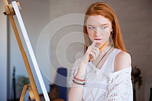 Pensive attractive female artist thinking near easel in drawing class