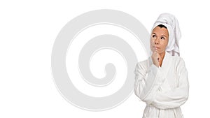 Pensive attractive middle aged woman in robe and towel on head thinking and looking to the side on white isolated background.