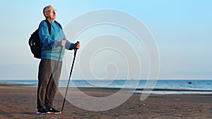 Pensive backpacker elderly man Scandinavian walking stick relaxing at sea beach contemplate sunset