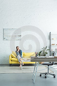 pensive barefoot girl sitting on sofa and looking away