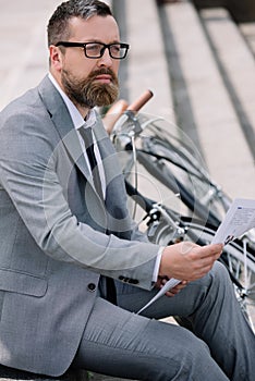 pensive bearded businessman reading newspaper on stairs