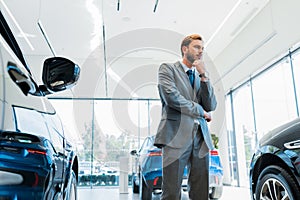 pensive bearded businessman standing near automobiles