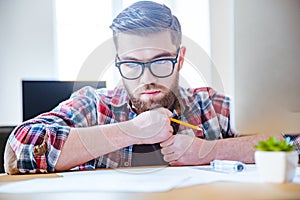 Pensive bearded engineer sitting at the table and creating blueprint