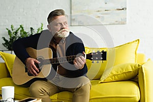 pensive bearded senior man playing guitar and looking away