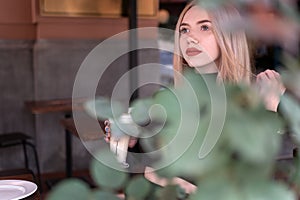 Pensive beautiful girl alone in cafe. Attractive blonde woman sits in coffee shop with cup of cappuccino coffee latte