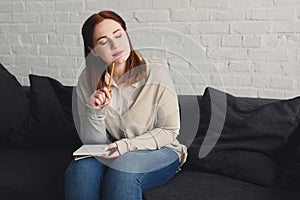 pensive beautiful girl with closed eyes touching chin with pencil