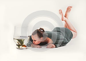 A pensive beautiful girl lies on the floor with an aquarium and looks at goldfish. Pet care concept