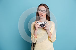Pensive beautiful girl with photocamera over blue background