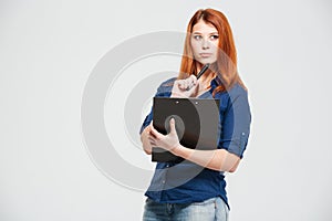 Pensive beautiful redhead young woman holding clipboard and thinking